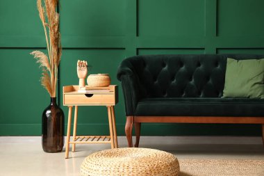 Yeşil duvarın yanında şık bir kanepe, puf ve masa.