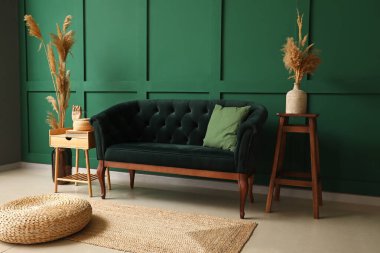 Yeşil duvarın yanında şık bir kanepe, puf ve masa.