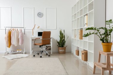 Modern çalışma odasının içi ve aydınlık duvarın yanında giysili raflar.