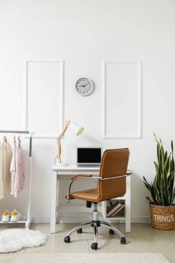 Modern dizüstü bilgisayarı olan işyeri ve ışık duvarının yanında giysileri olan raflar.