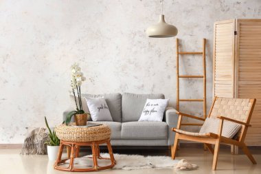 Rahat bir kanepe, koltuk ve masa. Odanın içindeki masada orkide çiçeği var.