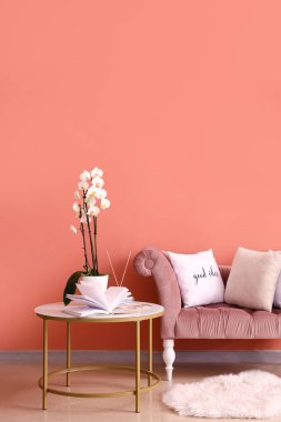 Book and beautiful orchid flower on table near color wall