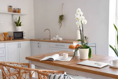 Yemek masasında lezzetli bir kahvaltı, dergi, dizüstü bilgisayar ve orkide var.