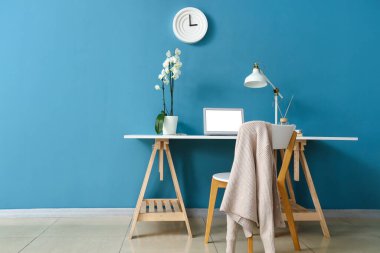 Modern dizüstü bilgisayar ve orkide çiçeğiyle rahat bir iş yeri. Odanın içindeki renkli duvarın yanında.