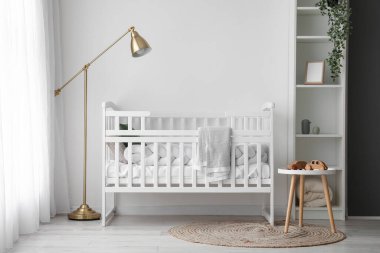 Interior of light nursery with baby crib, lamp and shelving unit