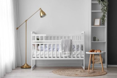 Interior of light nursery with baby crib, lamp and shelving unit