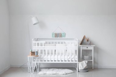 Bebek beşiği, lamba ve masalarla aydınlık çocuk odasının içinde.