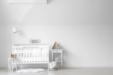 Interior of light nursery with baby crib, lamp and tables