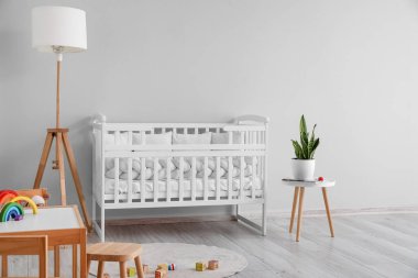 Interior of light nursery with baby crib, lamp and table
