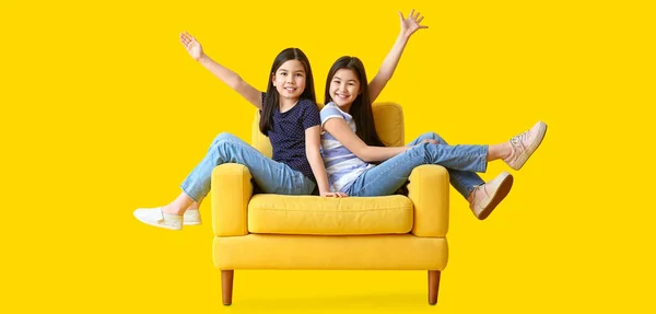 幸せな小さな姉妹座っていますアームチェアに対して黄色の背景 — ストック写真