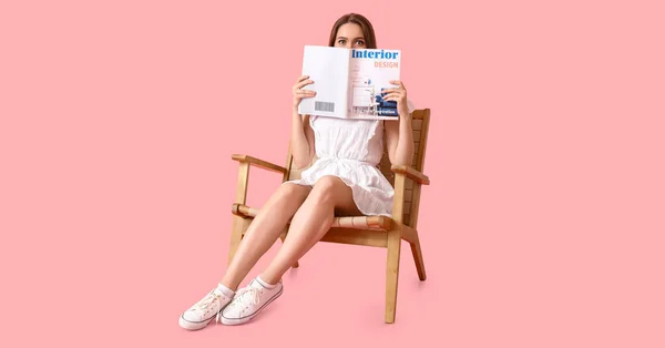 驚いた若い女性読書雑誌で木製アームチェアでピンクの背景 — ストック写真