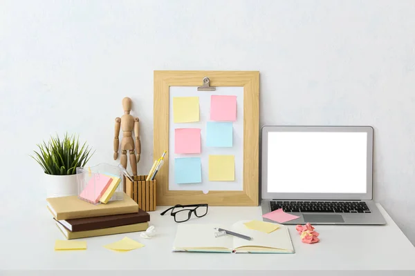 Workplace with laptop, mood board, sticky notes, notebooks, eyeglasses and decor near white wall