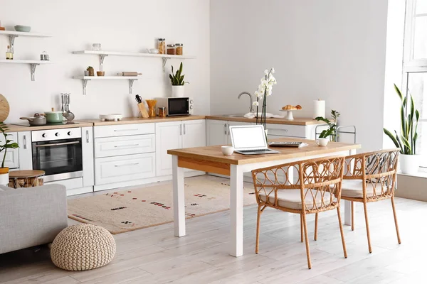 Modern interior of light kitchen with laptop on dining table
