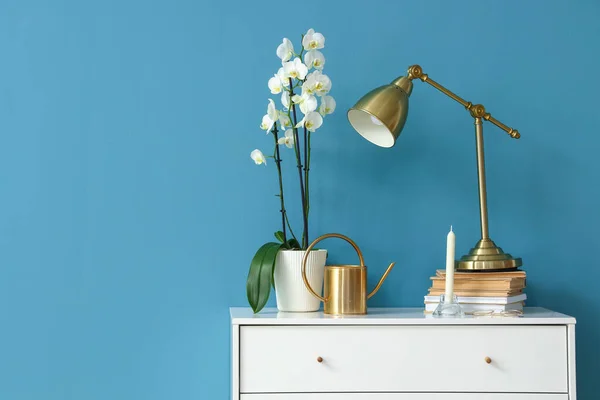 Orchid Flowers Lamp Watering Can Books Chest Drawers Blue Wall — стоковое фото