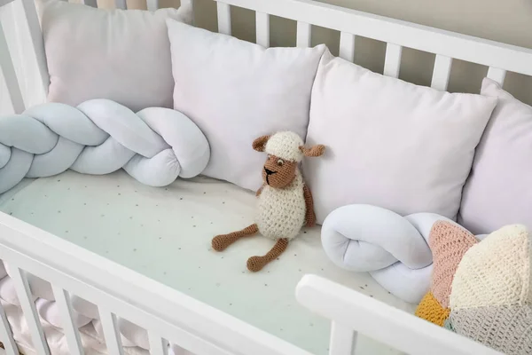 Baby crib with pillows and toy near light wall, closeup