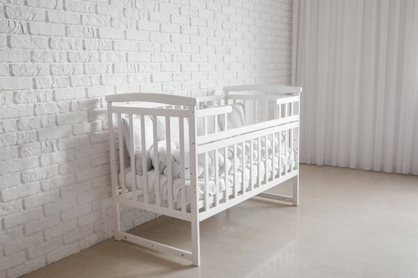 Baby crib with pillows near white brick wall