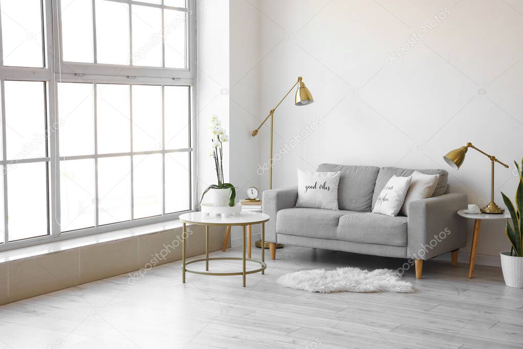 Interior of light living room with comfortable sofa near white wall
