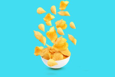 Bir sürü lezzetli patates cipsi açık mavi arka planda kaseye düşüyor.