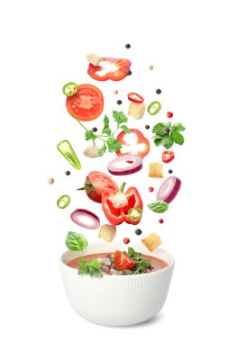 Bir kase lezzetli domates çorbası ve beyaz arka plana dökülen taze malzemeler.