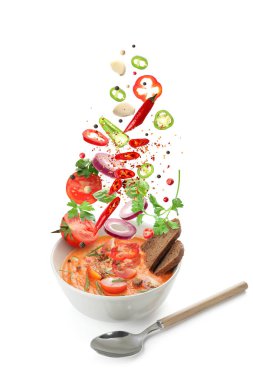 Bir kase lezzetli domates çorbası ve beyaz arka plana dökülen taze malzemeler.