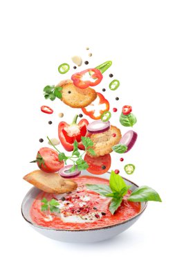 Bowl of tasty tomato soup with falling fresh ingredients on white background