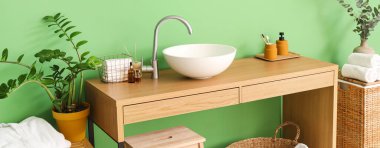 Banyoda yeşil duvarın yanında lavabo ve banyo malzemeleri olan bir masa.