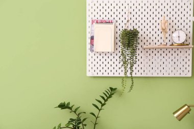 Pegboard with stylish decor, houseplants and notebook on color wall