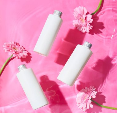 Renkli arka planda su içinde güzel Gerbera çiçekleri ve kozmetik ürünleri şişeleri