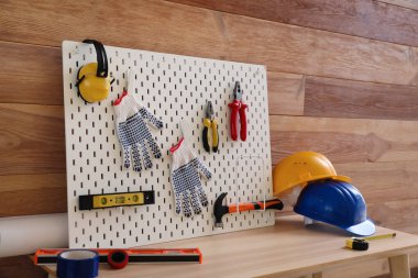Pegboard with modern tools on desk near wooden wall