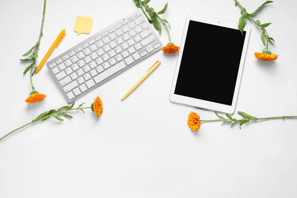 Tablet with computer keyboard, pens, sticky note and flowers on white background