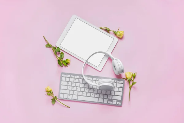 Tablet with computer keyboard, headphones and roses on pink background