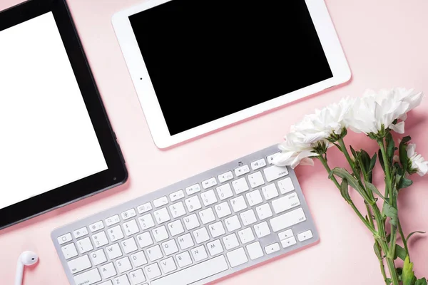 Tablet computers with keyboard and flowers on pink background