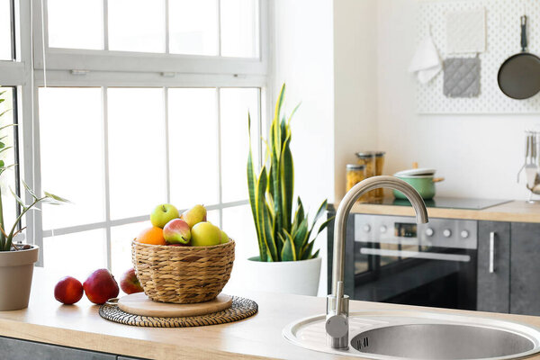 Wicker basket with delicious fruits on counter in modern kitchen
