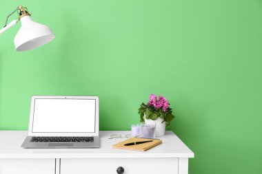 Renk duvarına yakın modern dizüstü bilgisayarı, lambası ve dekoru olan işyeri