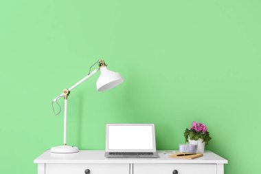 Renk duvarına yakın modern dizüstü bilgisayarı ve lambası olan işyeri