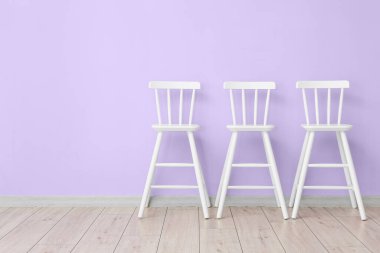 İç odada, mor duvarın yanında beyaz sandalyeler.