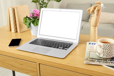 Workplace with modern laptop, mobile phone, cup and magazines in room