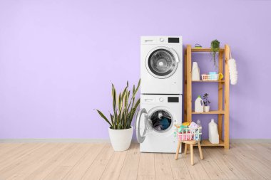 Modern kurutma, çamaşır makineleri, çamaşır sepeti ve oda içi menekşe duvarının yanındaki raf ünitesi.