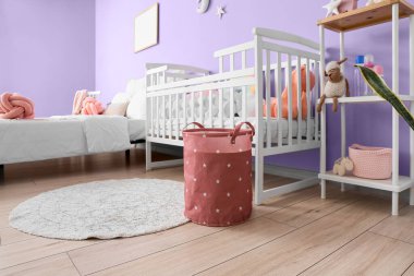 Bebek beşiği ve menekşe duvarın yanında rahat bir yatak.