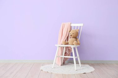 Oyuncak ayı ve yumuşak ekose sandalyenin üzerinde. İç odada, menekşe duvarın yanında.