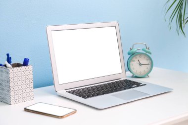 Modern dizüstü bilgisayar, cep telefonu ve alarm saati renk duvarının yanındaki masada.