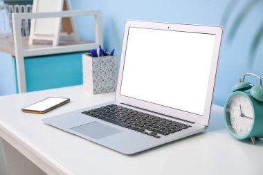 Modern dizüstü bilgisayar, cep telefonu ve alarm saati renk duvarının yanındaki masada.