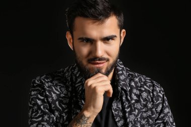 Genç adam karanlık arka planda sakala dokunuyor.