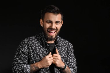 Duygusal sakallı adam koyu arkaplanda gömlek ayarlıyor.