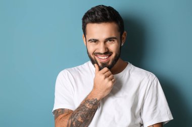 Gülümseyen modaya uygun adam mavi arka planda sakala dokunuyor.