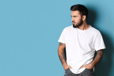 Yakışıklı sakallı adam ellerini cebinde tutuyor ve mavi arka plana bakıyor.