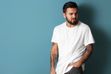 Yakışıklı sakallı adam mavi arka planda ellerini cebinde tutuyor.