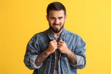 Sarı arka planda kot ceket giyen gülümseyen sakallı adam.