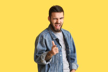 Gülümseyen adam izleyiciyi işaret ediyor ve sarı arka planda göz kırpıyor.