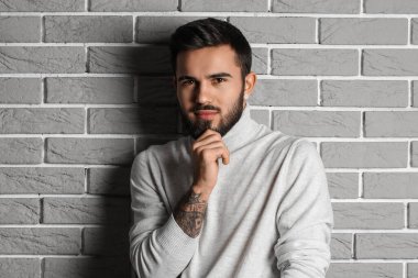 Gri tuğlalı arka planda modaya uygun sakallı adam.